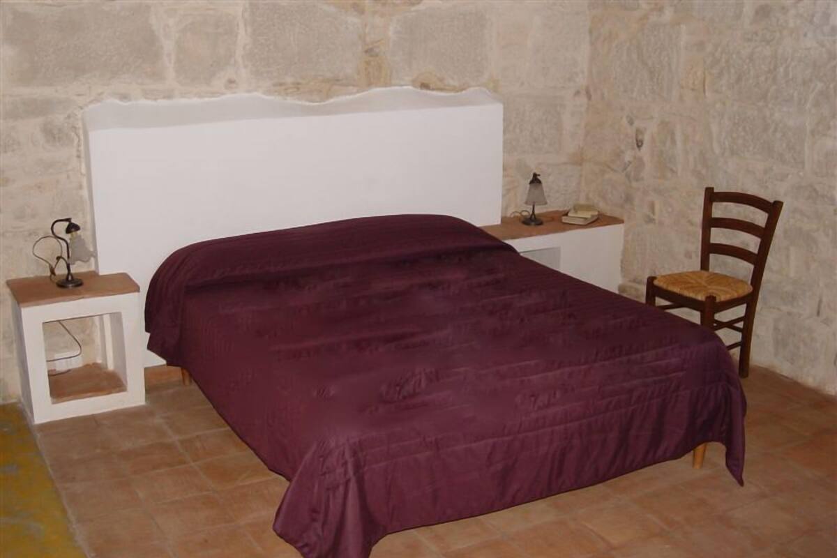A bedroom with a bed, a nightstand, a chair, and a small table with a lamp.