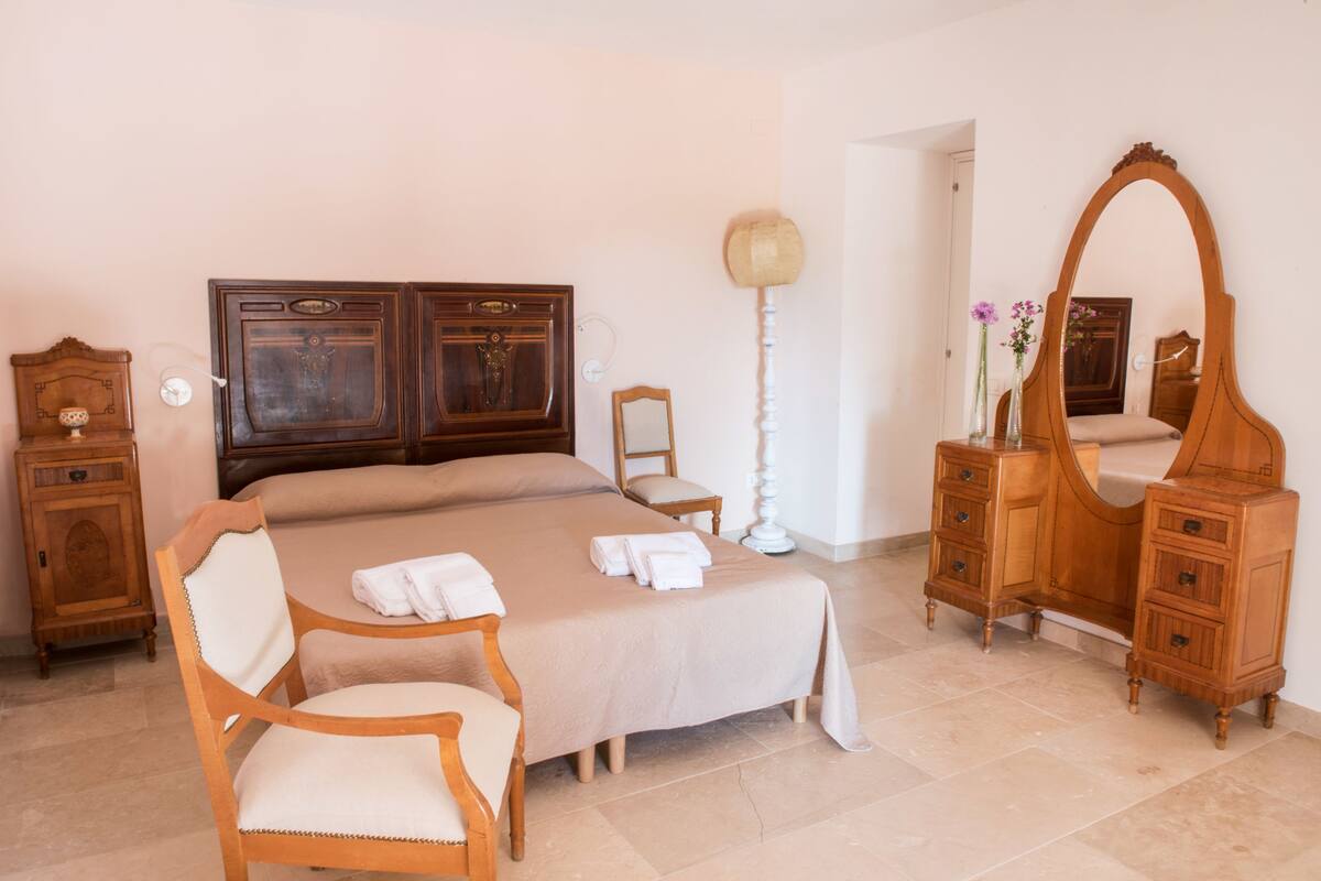 A bedroom with a large bed, wooden furniture, a chair, a dresser, and a mirror.
