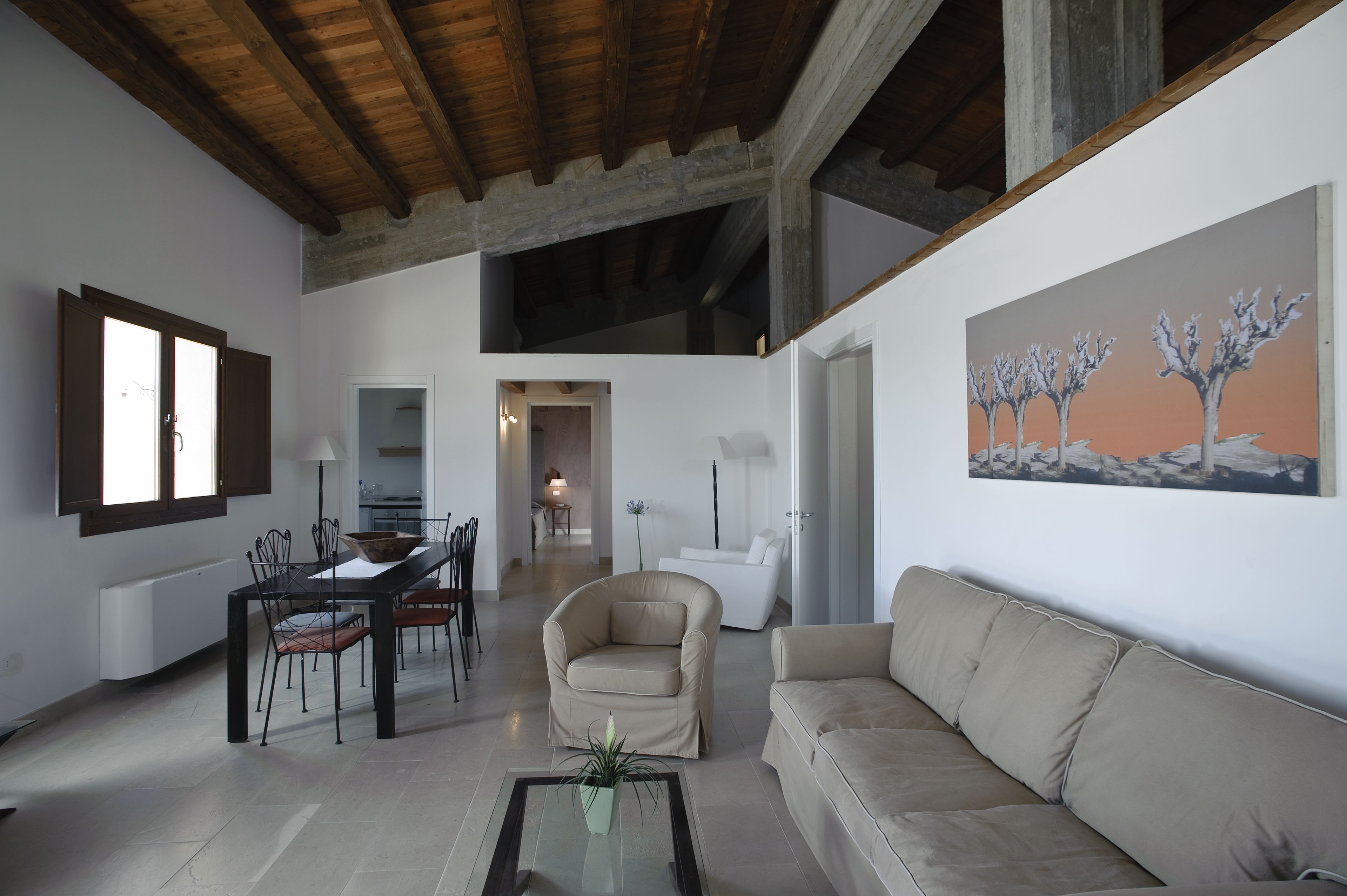 A spacious living area with a dining table, chairs, a sofa, and a painting on the wall.
