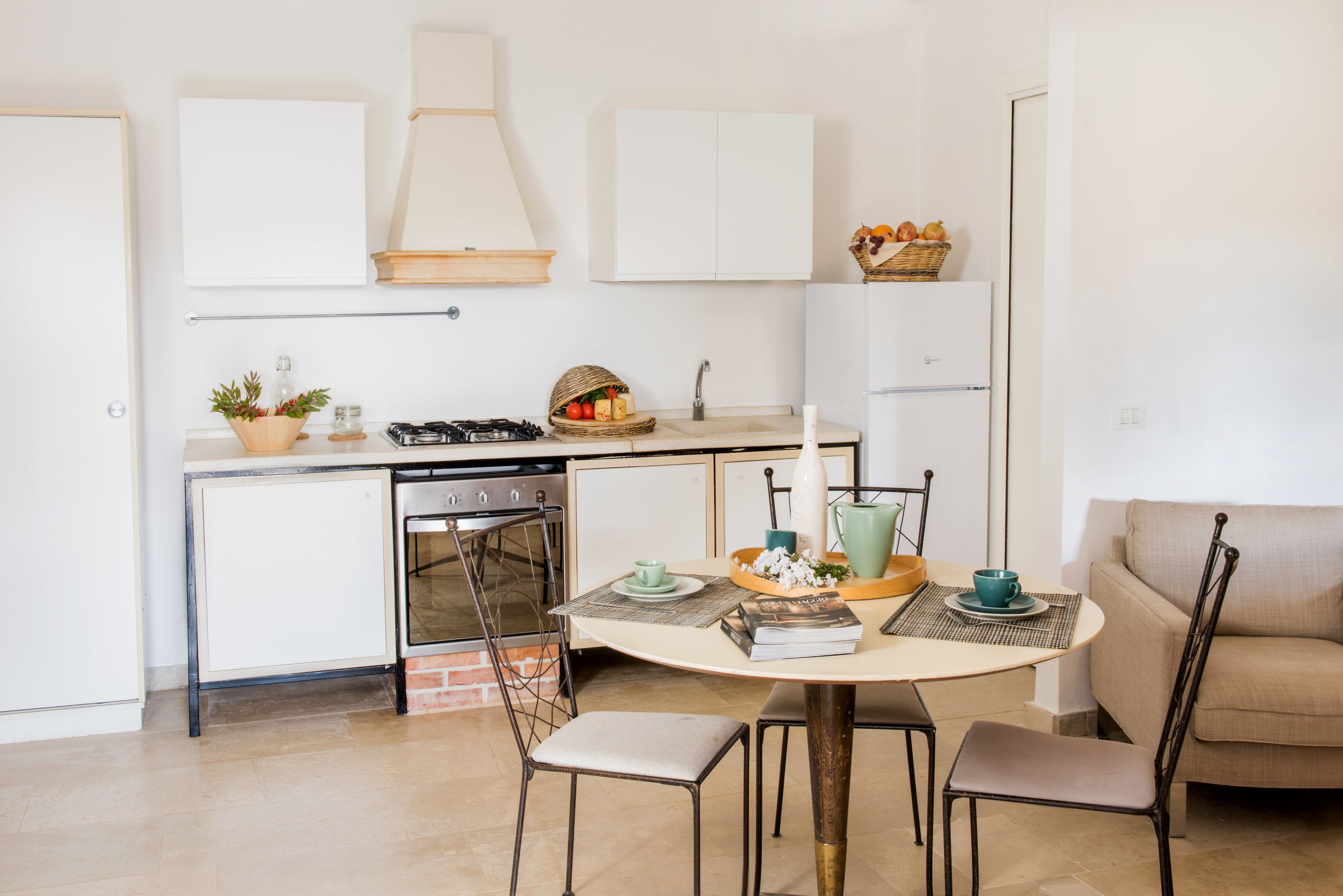 A compact kitchen with a dining area, featuring a round table, chairs, a small stove, and a refrigerator.