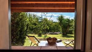 A view from a window of a room with a wooden ceiling, a table with a basket of fruit, and two chairs. - Relais Parco Cavalonga (Ragusa)
