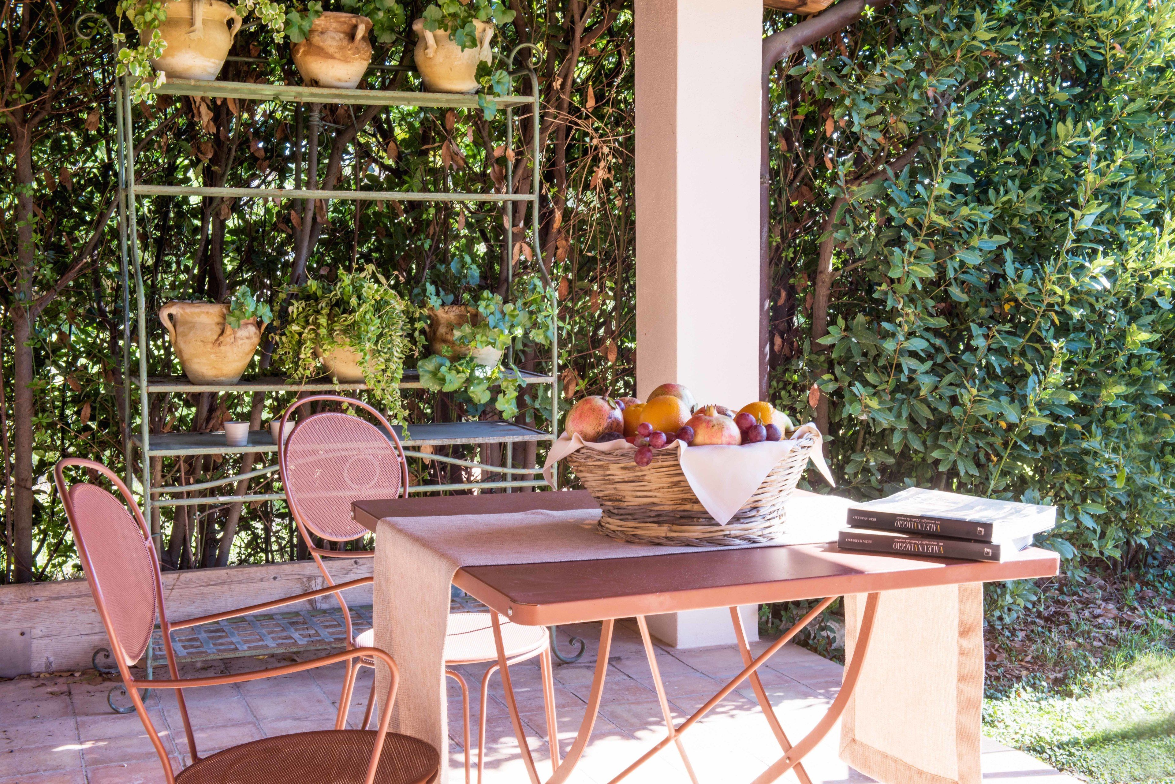 A patio area with a table, chairs, a basket of fruit, and a metal shelf with pots.