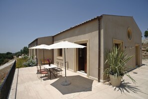 Ein Gebäude mit einer Terrassenfläche, ausgestattet mit einem Tisch, Stühlen, einem weißen Sonnenschirm und einem Blumentopf.