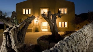A two-story house with a stone facade, multiple windows, and a well-lit entrance. - Relais Parco Cavalonga (Ragusa)