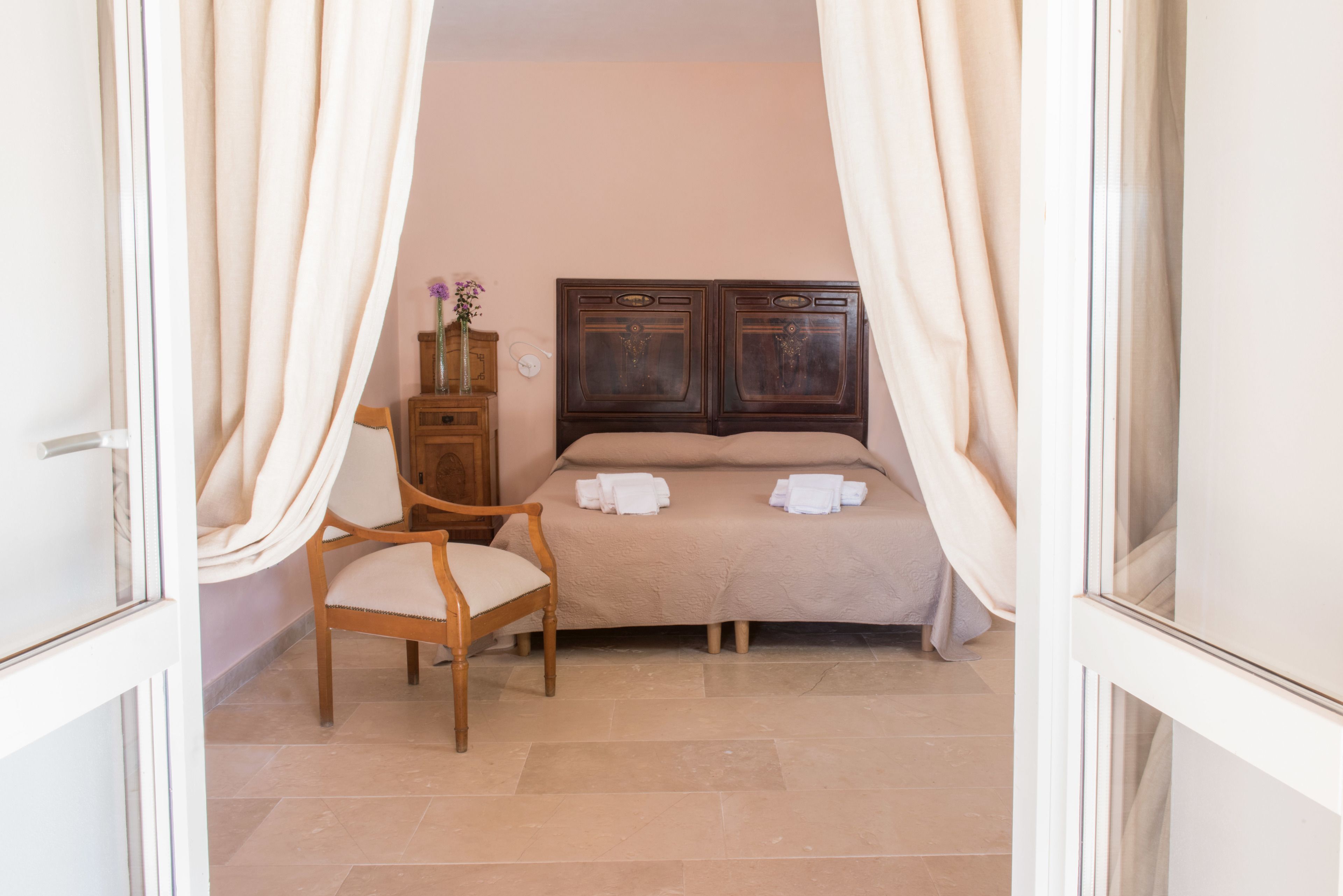 Un dormitorio con cama, una silla, una mesita de noche y un florero con flores.