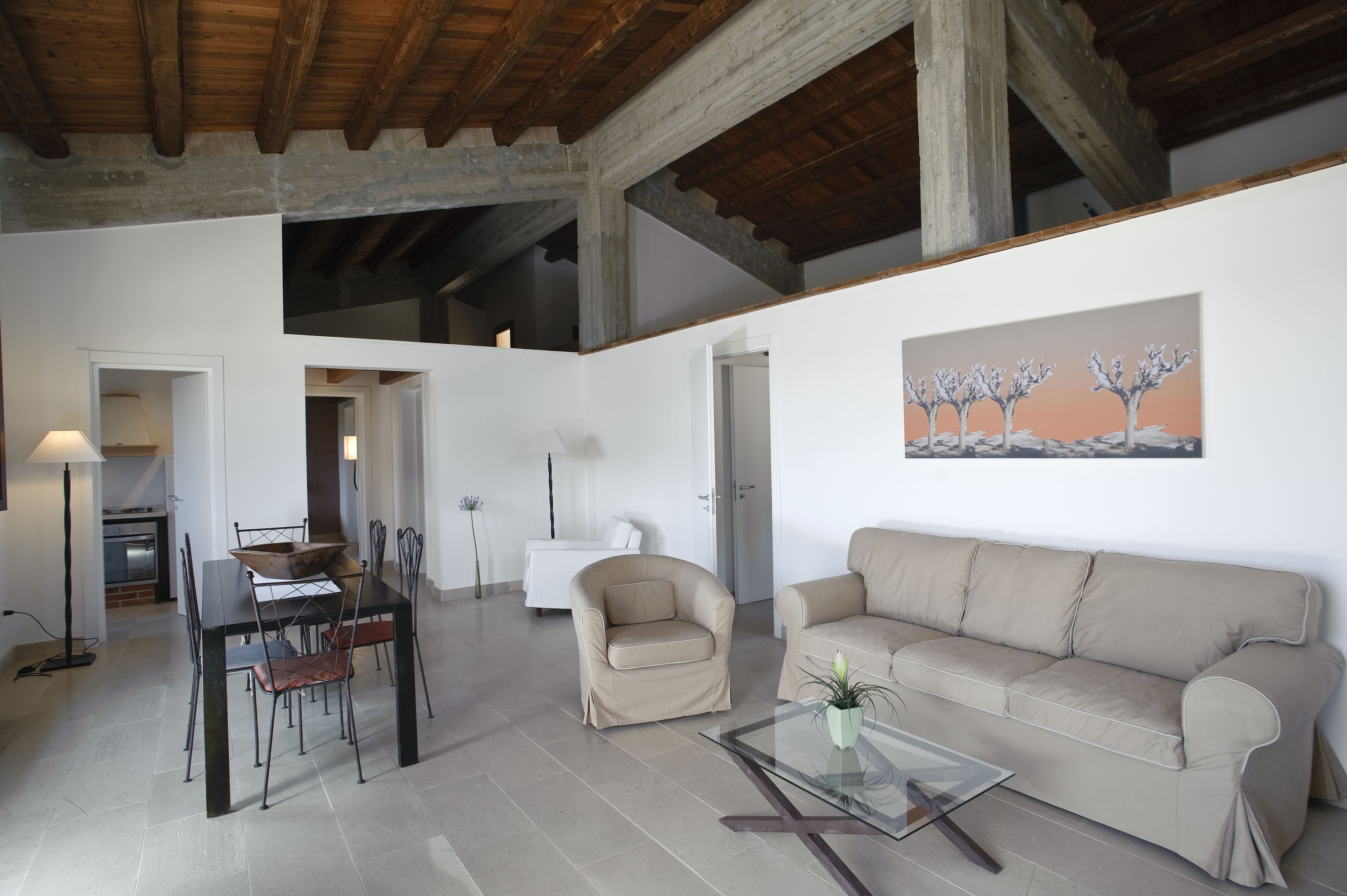 A spacious living area with a dining table, chairs, a sofa, and a painting on the wall.