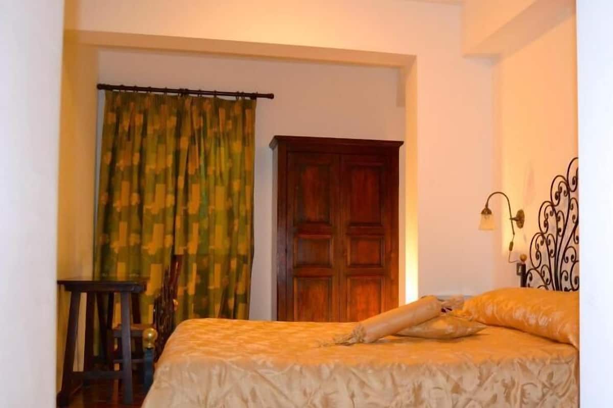 Un dormitorio con cama, un armario de madera, una cortina y una mesita con silla.