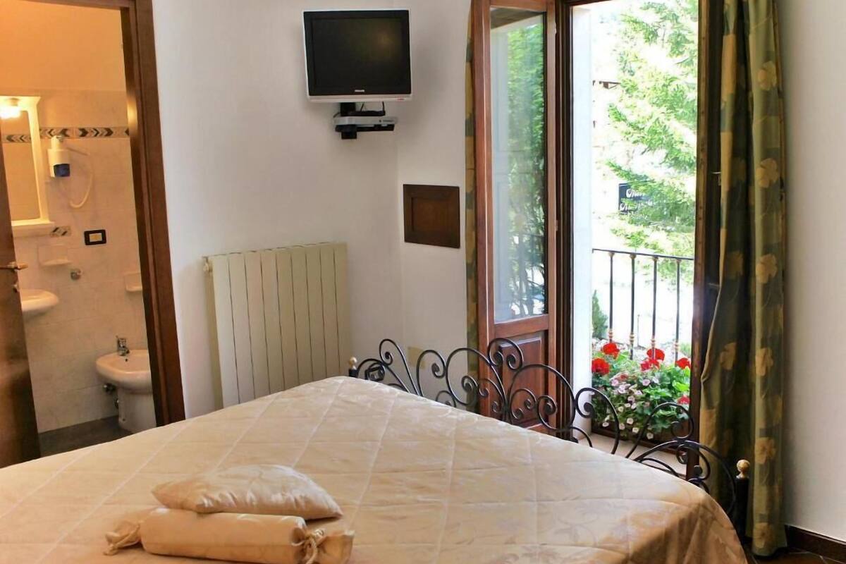 Un dormitorio con cama, televisor montado en la pared y vistas a un balcón con flores.