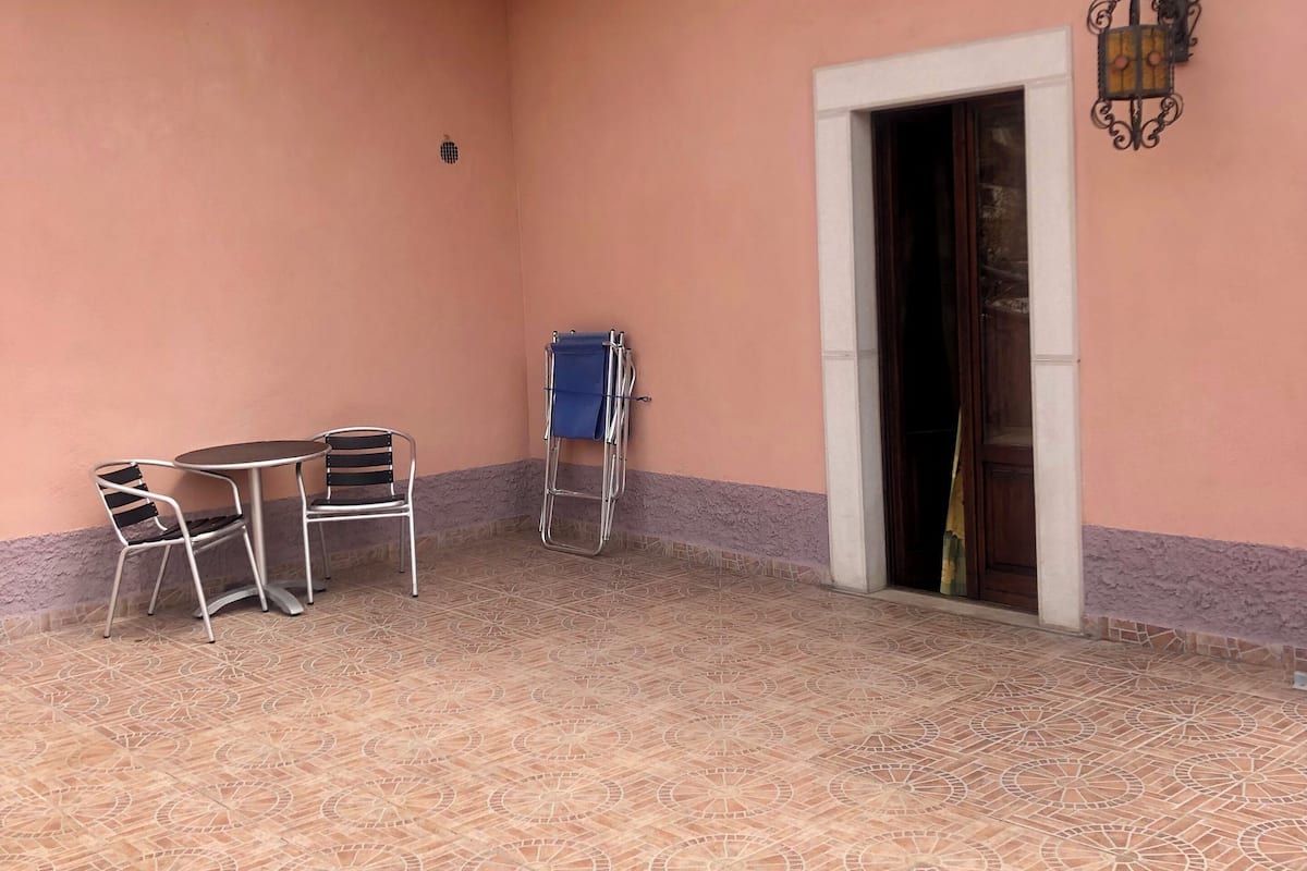 Un patio techado con suelo de baldosas, una mesa con sillas y una silla plegable azul.