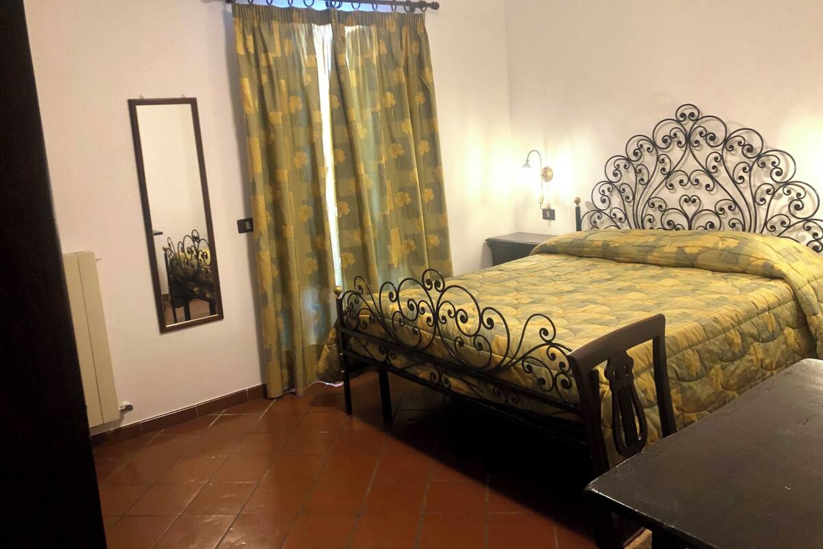 Un dormitorio con una cama, una mesita de noche, un espejo y una cortina.
