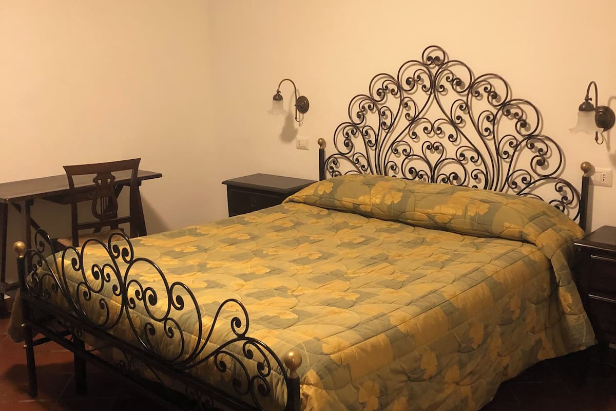 Una cama individual con colcha estampada, una mesita de noche, una lámpara de pared y una pequeña mesa con una silla.