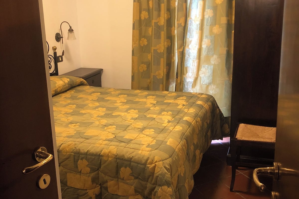 Una habitación con cama, mesita de noche, lámpara, silla y armario.
