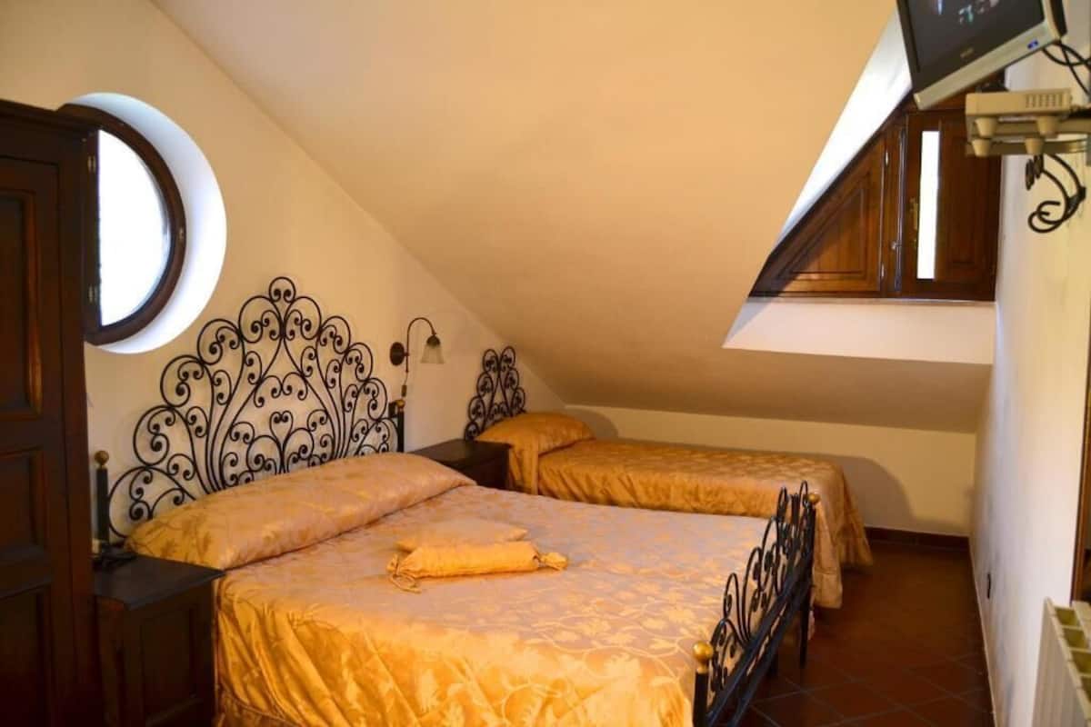 Un dormitorio con dos camas, un ventanal circular y techo inclinado.