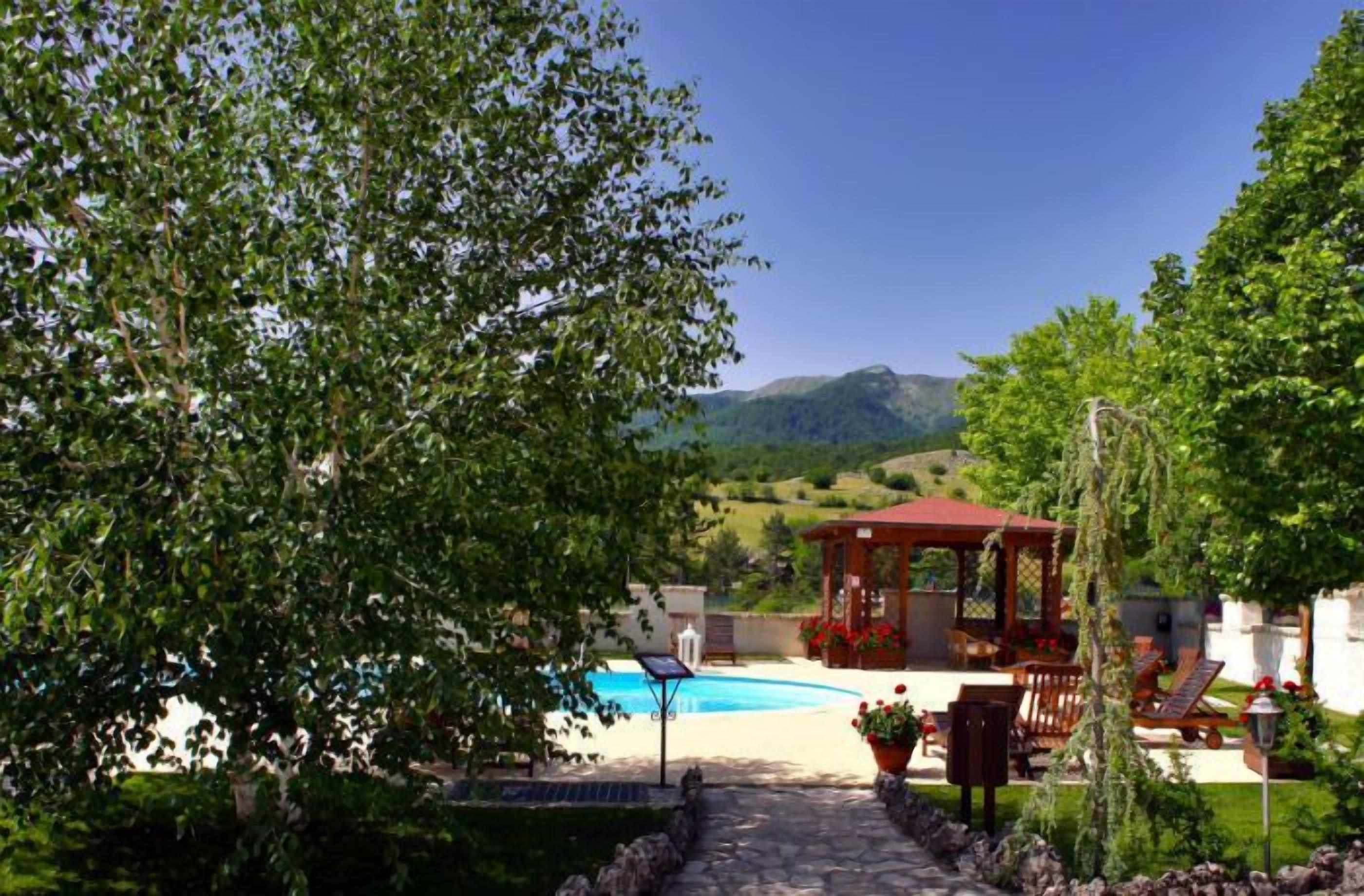 A pool area with a gazebo, seating, and a view of hills.