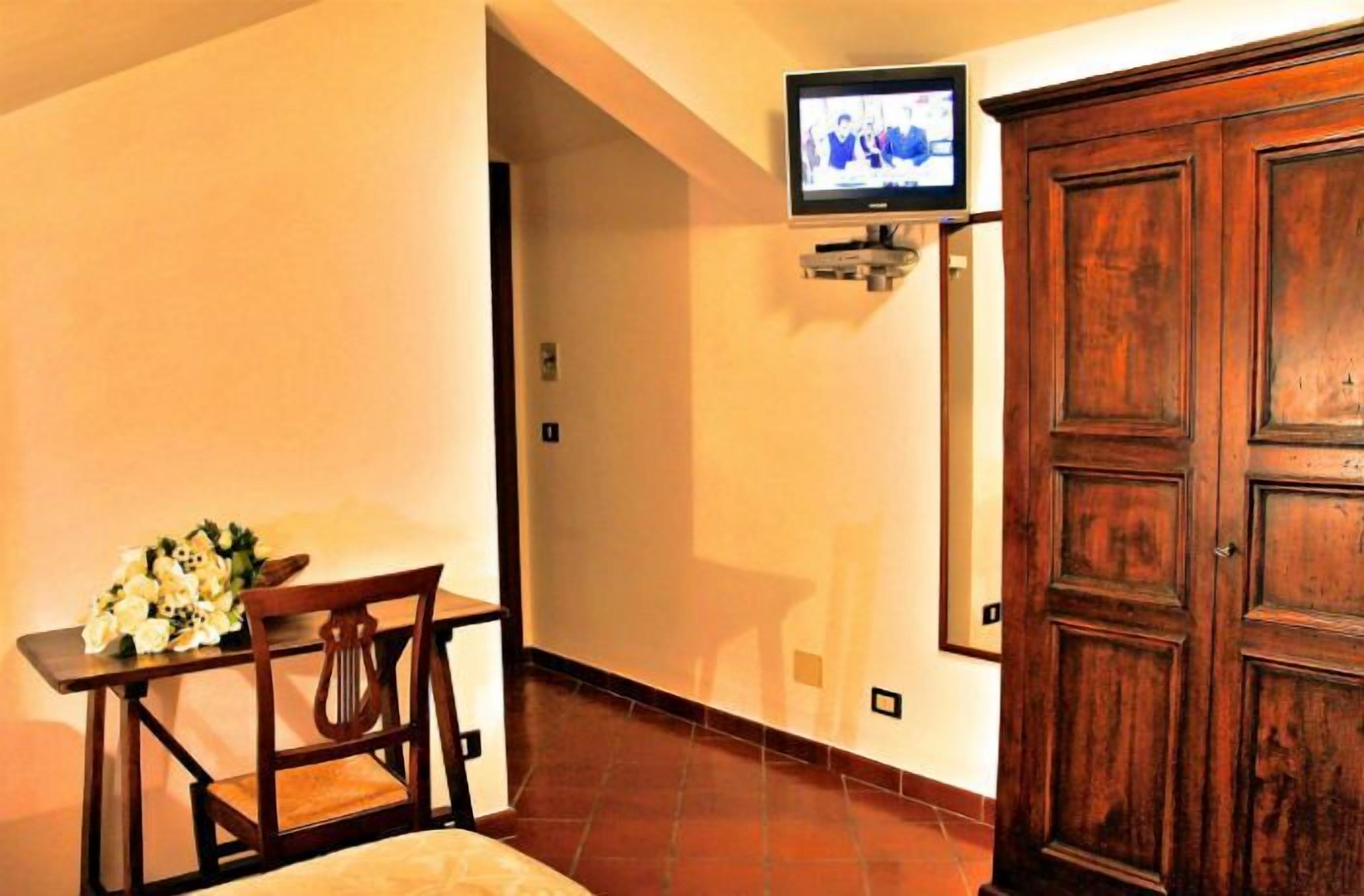 Una habitación con un armario de madera, un televisor montado en la pared y una mesa con un arreglo floral.