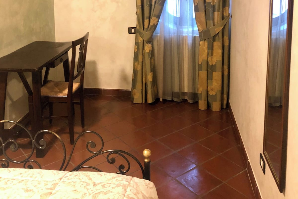 Una habitación con cama, una mesa con sillas, un televisor montado en la pared y una ventana con cortinas.