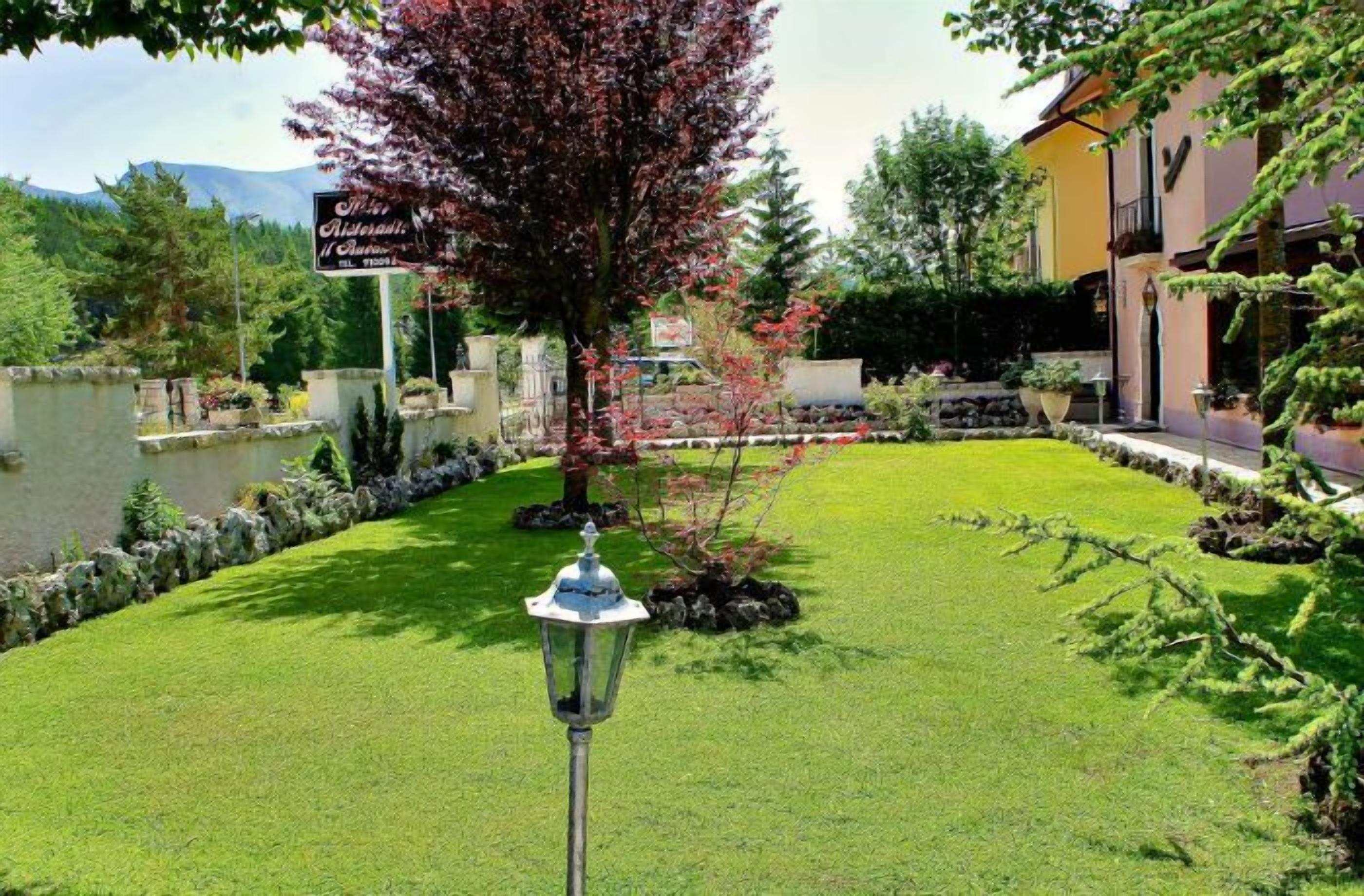 A well-maintained garden with a pond, a sign for 'Hotel Restaurant Il Surrano', and a lamp post.