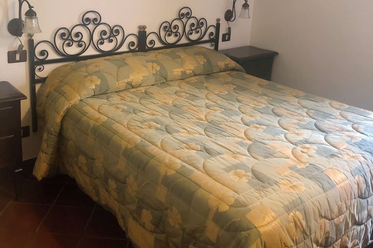 Una cama individual con colcha estampada, cabecero de metal negro y dos lámparas fijadas a la pared.