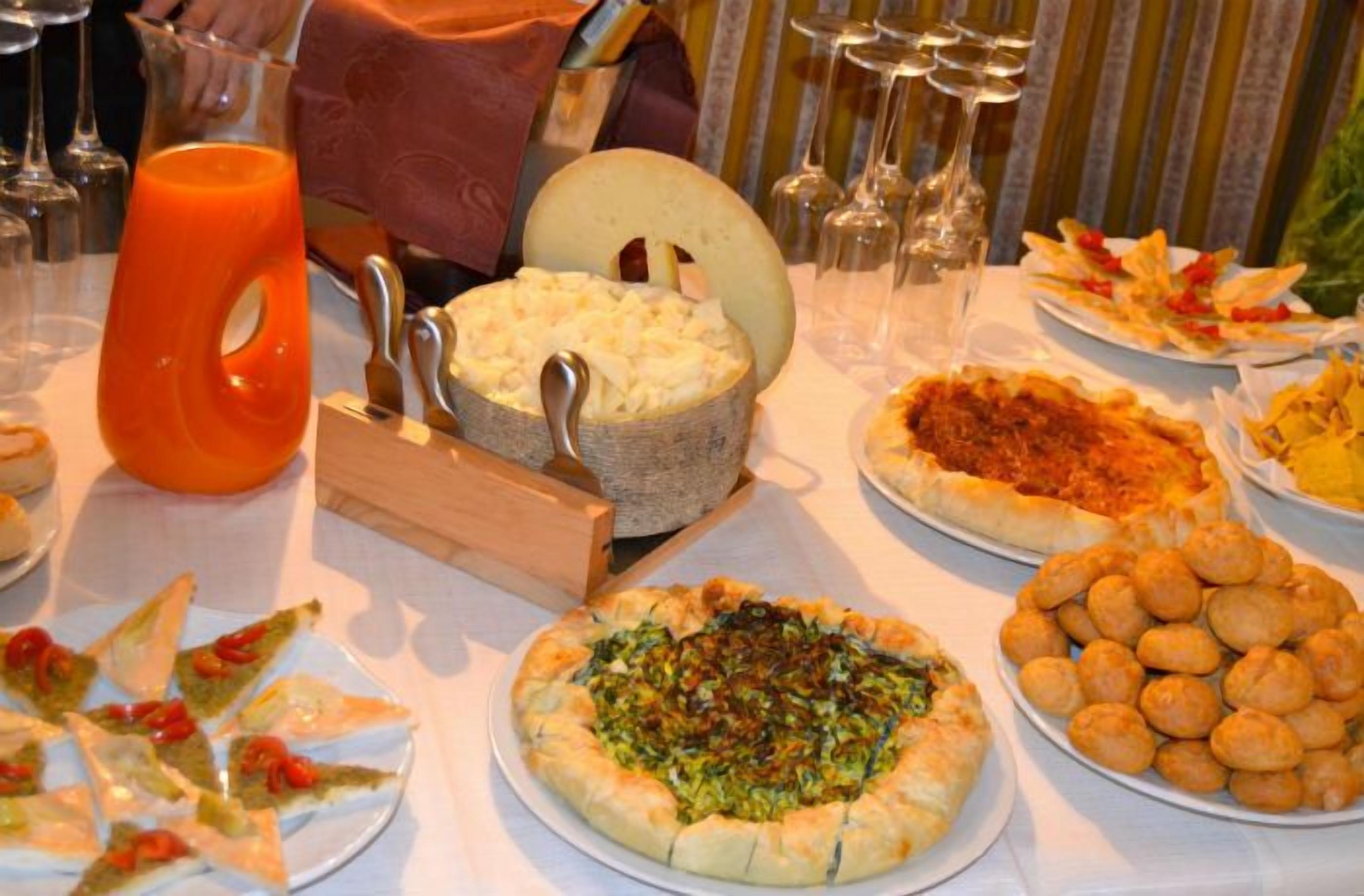 A buffet table with various dishes including pizza, a cheese wheel, and a pitcher of orange juice.