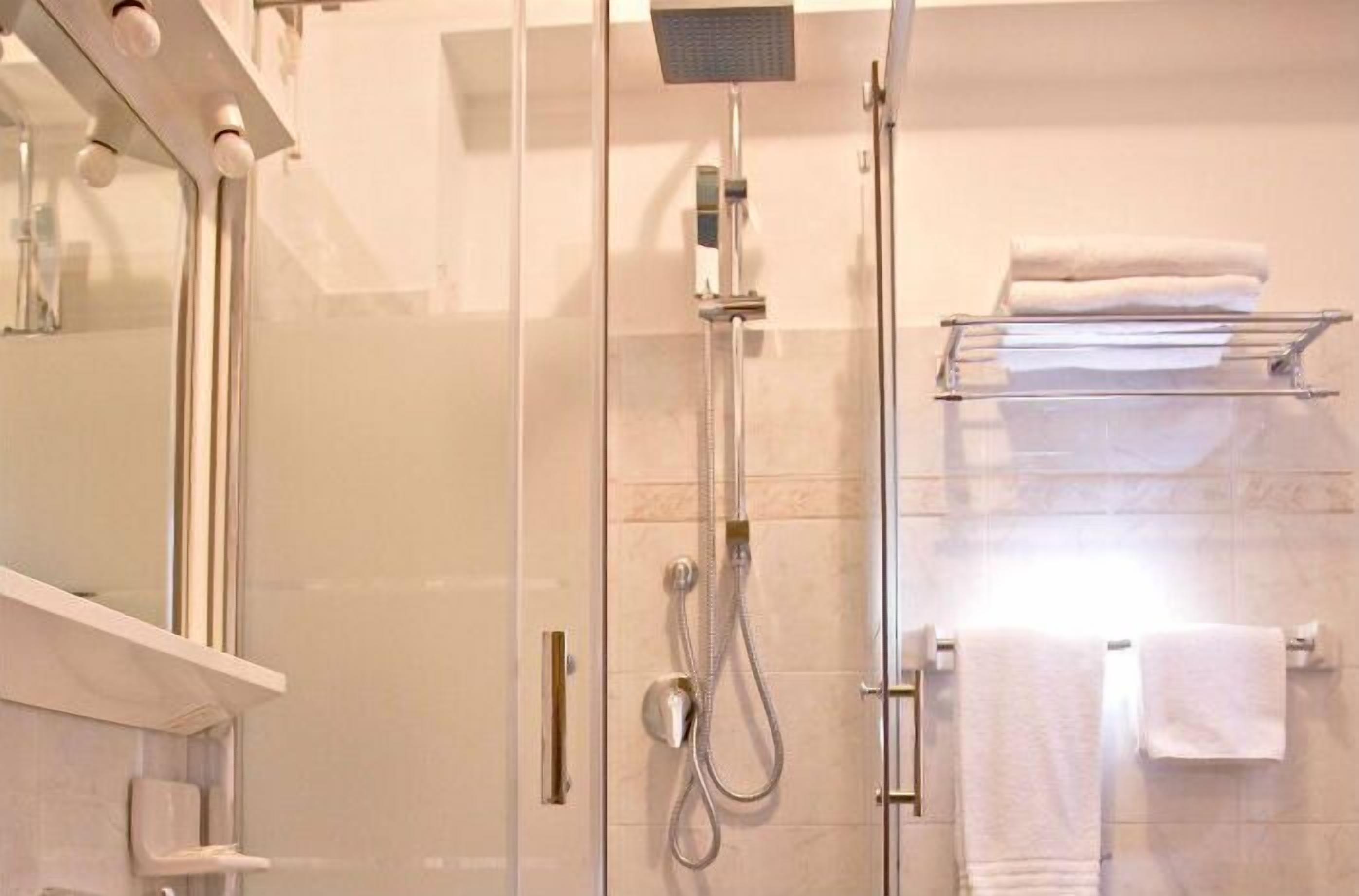 Um banheiro moderno com chuveiro em cabine de vidro, porta-toalhas branco e espelho.