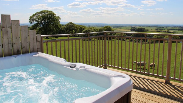 A hot tub on a wooden deck with a view of a grassy field and trees. - Garth Cottage (Brampton)