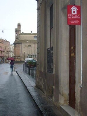 A narrow street with a person walking, a red sign for PRISCILLA Bed & Breakfast, and historic buildings. - Bed and Breakfast Priscilla (Regalbuto)