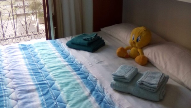 A hotel room with a bed, a window with curtains, a balcony, and a stuffed toy on the bed. - Bed and Breakfast Priscilla (Regalbuto)