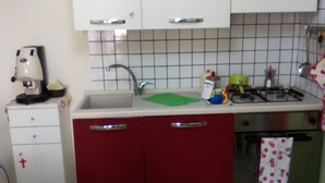 A kitchen with white cabinets, a red countertop, a sink, a stove, and a clock on the wall. - Bed and Breakfast Priscilla (Regalbuto)