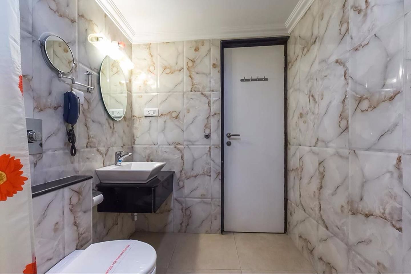 A bathroom with a marble wall, a sink, a toilet, and a door with a sign.