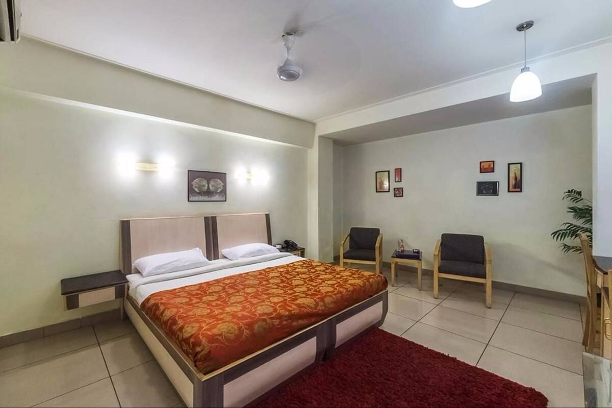 A bedroom with a bed, bedside tables, a red rug, two chairs, a small table, and a ceiling fan.