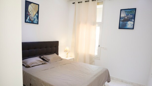 A bedroom with a bed, a nightstand, a lamp, and two paintings on the walls. - Charmin & Trendy Apartment Marsa Beach (La Marsa)
