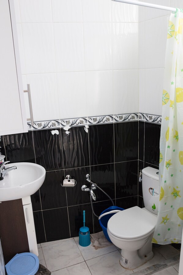 A bathroom with a white sink, black and white tiled walls, a white toilet, and a blue bucket.