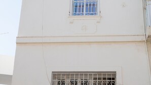 A building with a satellite dish, an air conditioning unit, barred windows, and a balcony with a white balustrade. - Charmin & Trendy Apartment Marsa Beach (La Marsa)