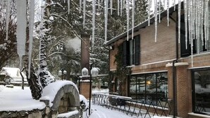 A snow-covered courtyard with a brick building, a stone fountain, and a snow-covered tree. - LH Hotel il Picchio (Pescasseroli)