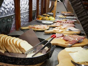 A buffet table with various food items including sliced bread, meats, and fruits. - LH Hotel il Picchio (Pescasseroli)