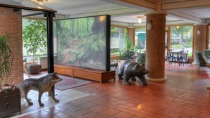 A spacious lobby with a large screen displaying a forest scene, a fireplace, and a stone pillar. - LH Hotel il Picchio (Pescasseroli)