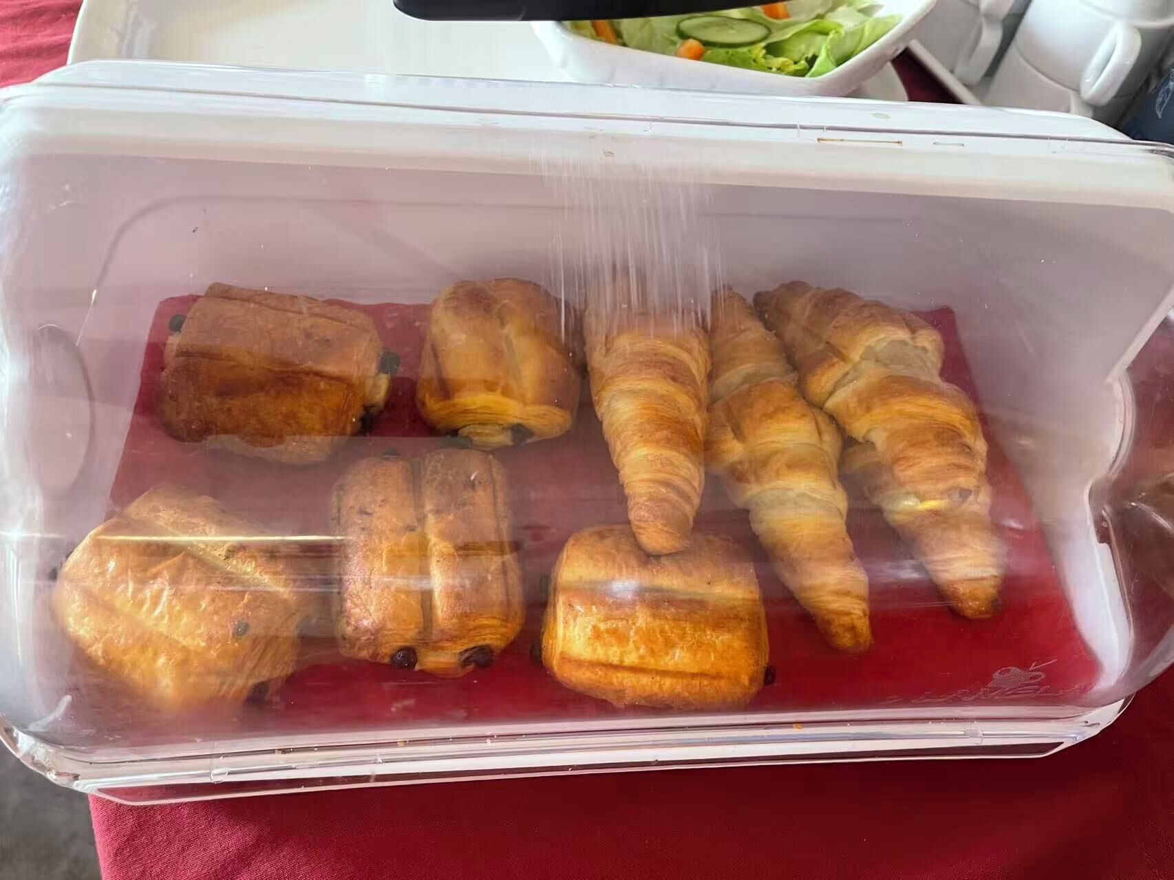 A plastic container with several croissants and a baguette.