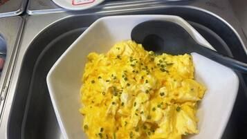 A bowl of scrambled eggs garnished with chives, placed on a tray with a black spoon.
