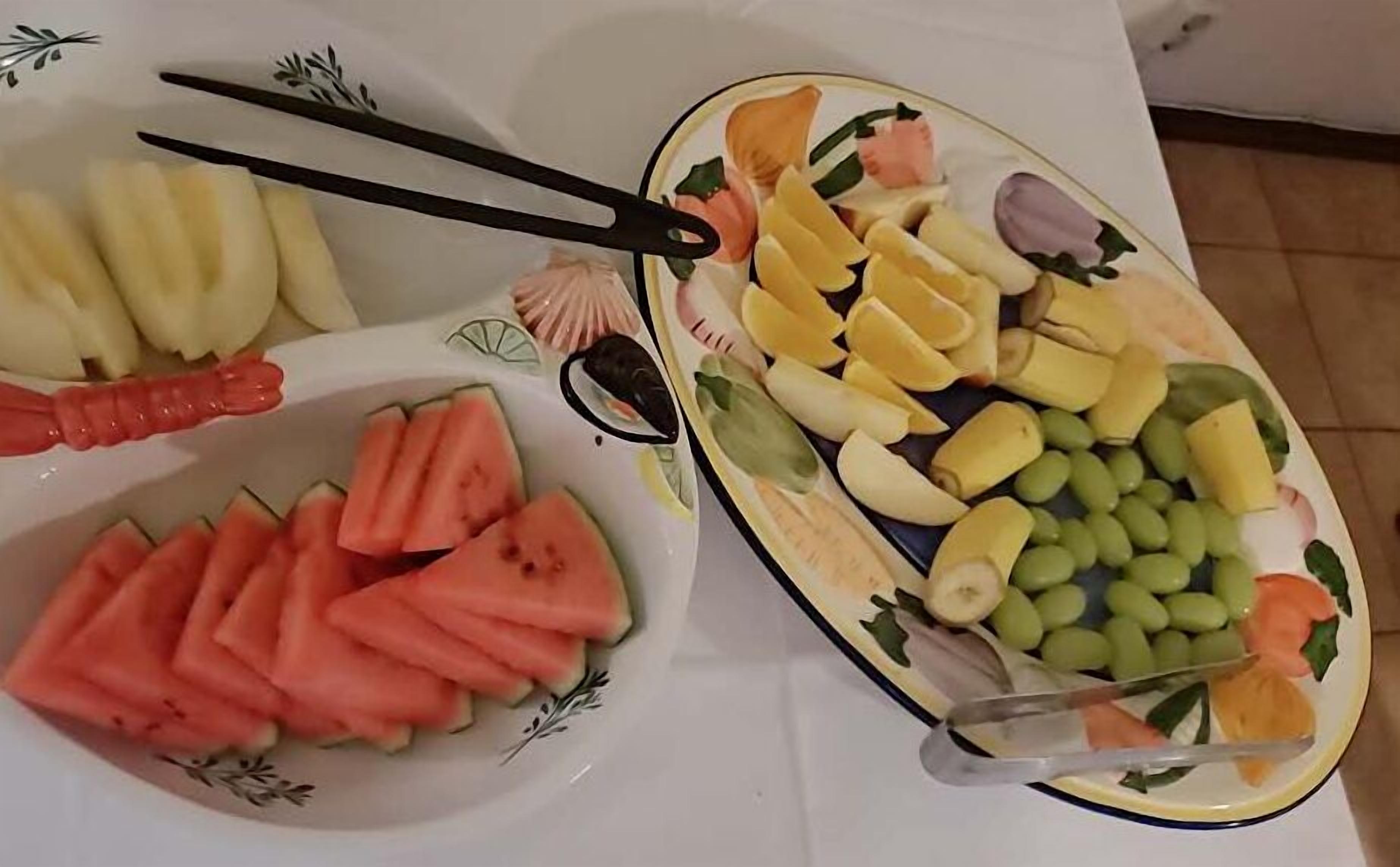 Una mesa con dos platos de frutas cortadas, incluyendo sandía, plátanos, uvas y otras variedades.