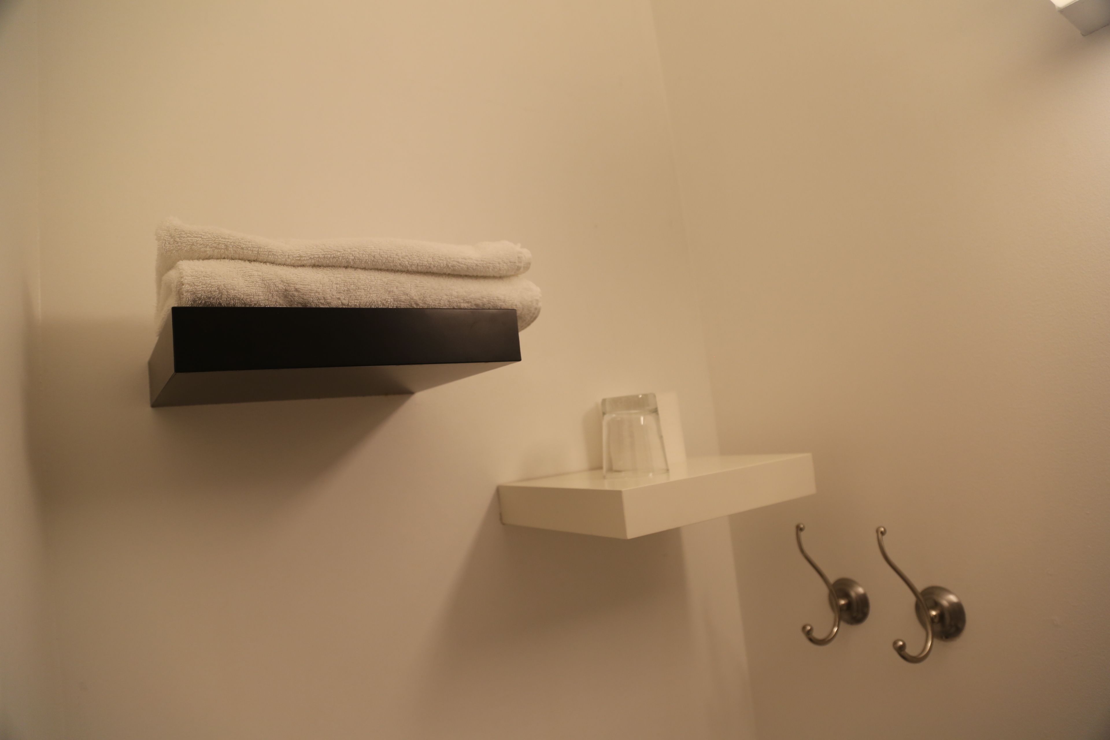 Un baño con un perchero con toallas dobladas, una repisa con un tarro de vidrio y dos ganchos metálicos.