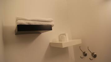 Un bagno con un portasciugamani pieno di asciugamani piegati, uno scaffale con un barattolo di vetro e due ganci metallici.