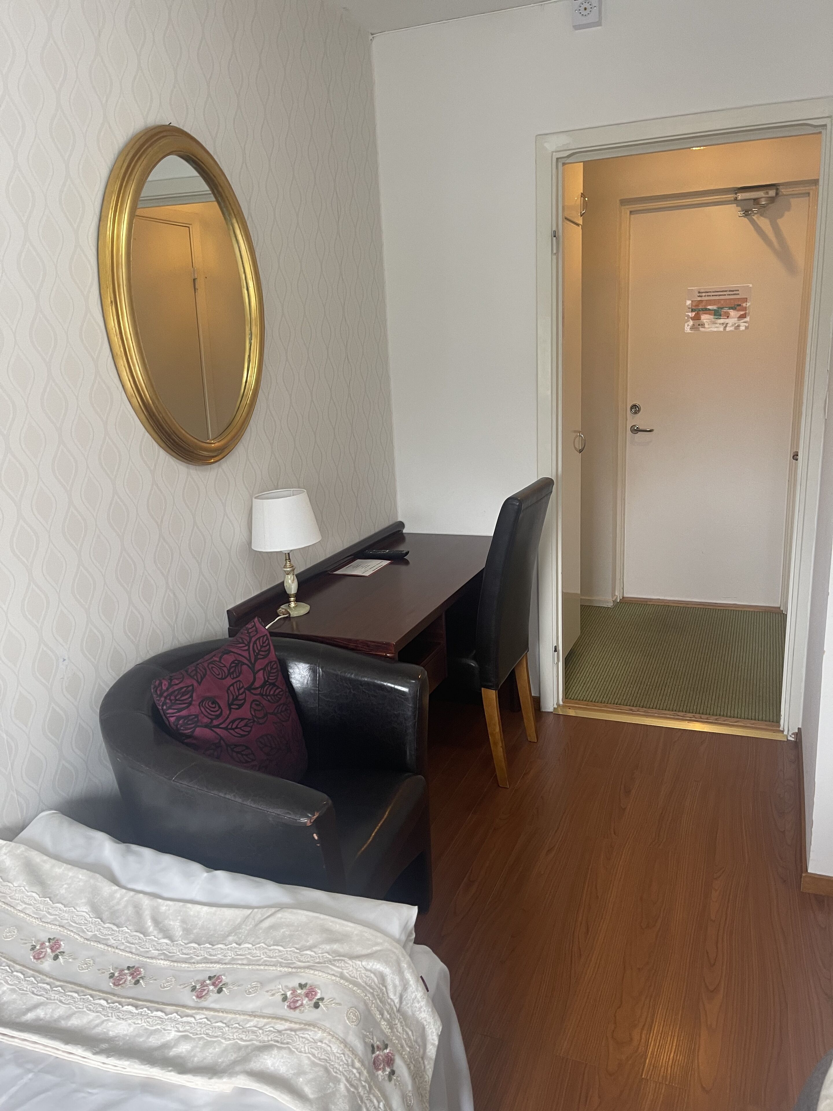 Et hotelværelse med seng, skrivebord, stol, spejl og dør.