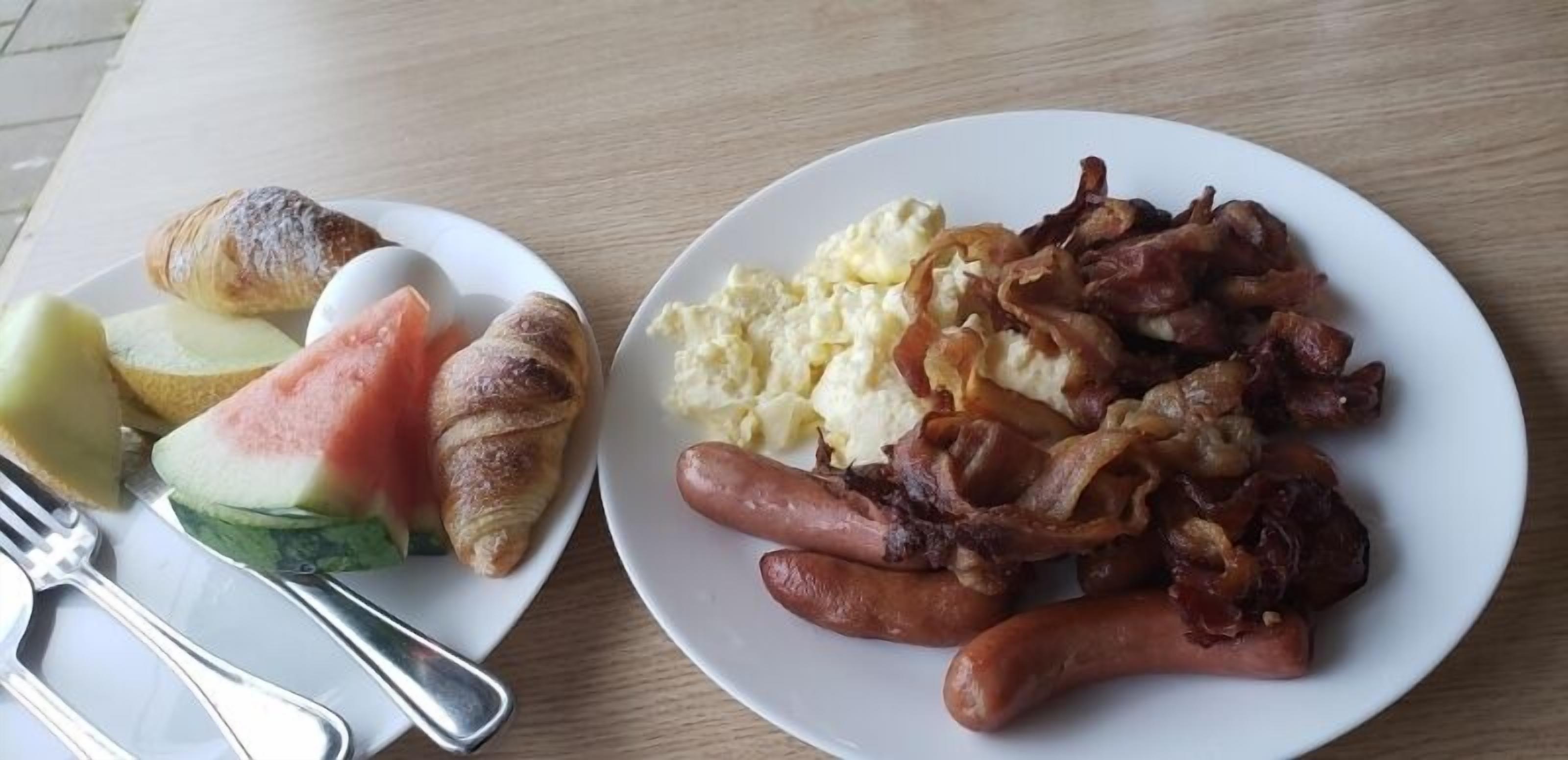 A breakfast plate with croissants, a croissant half, and a plate of sausages, bacon, and scrambled eggs.