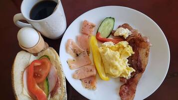 A breakfast plate with eggs, bacon, and vegetables, and a cup of coffee on the table.