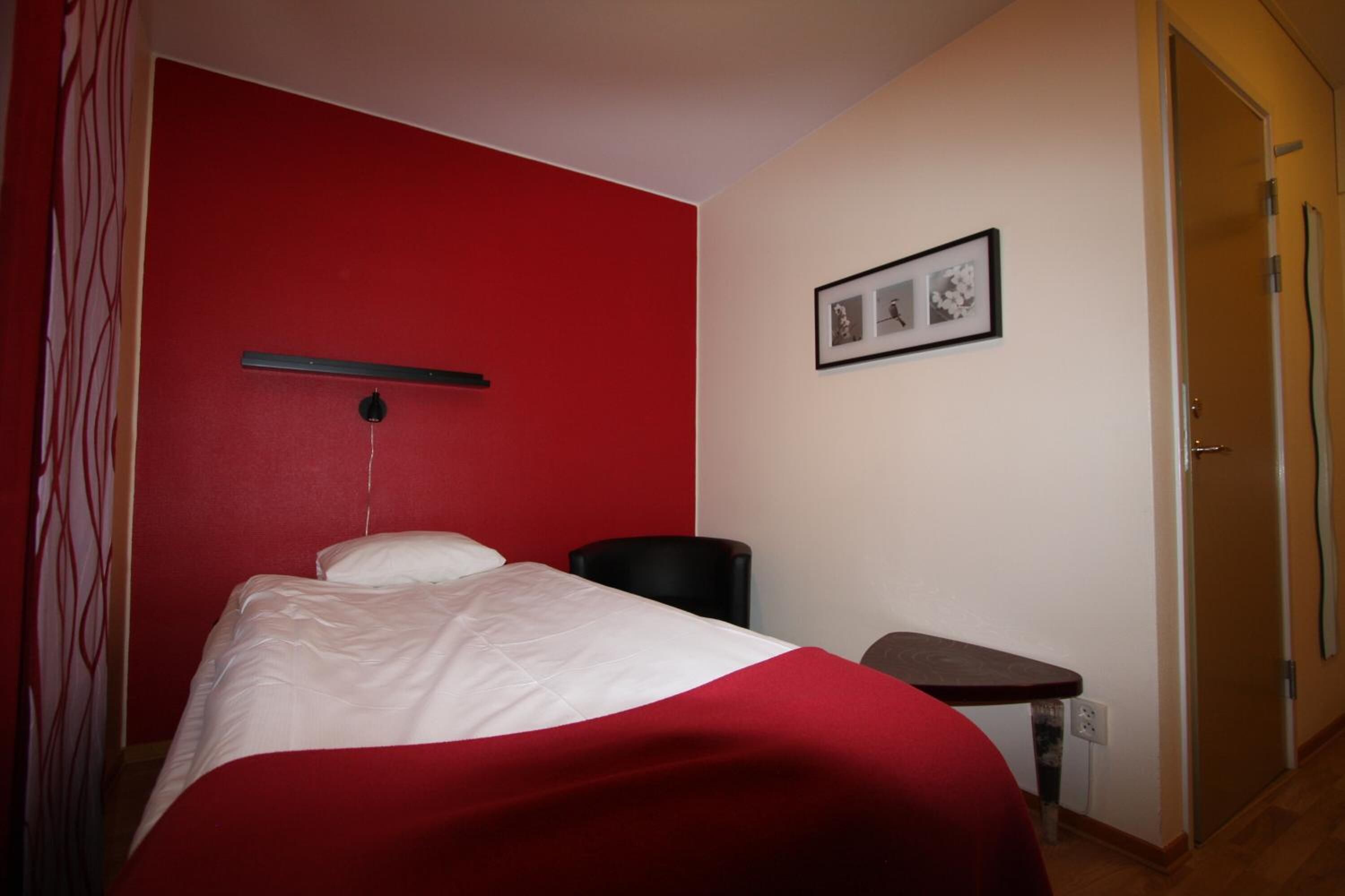 Une chambre d’hôtel avec un mur d’accent rouge, un lit avec une literie blanche, une petite table et un tableau au mur.