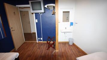 Ett hotellrum med trägolv, en tv som är monterad på väggen, ett litet bord, ett handfat och en papperskorg.