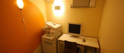 Ein kleiner Büroraum mit Schreibtisch, Computer, Drucker und Stuhl.