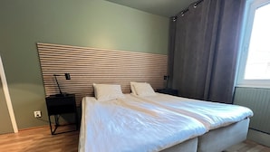 Un dormitorio con una cama grande, una mesita de noche, una lámpara y una ventana con cortinas.