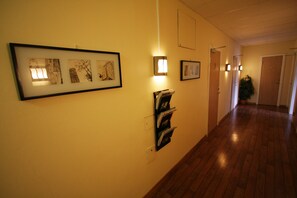 A hallway with framed artwork on the walls, a magazine rack, and a potted plant. - Hotell Linnéa (Ljungby)