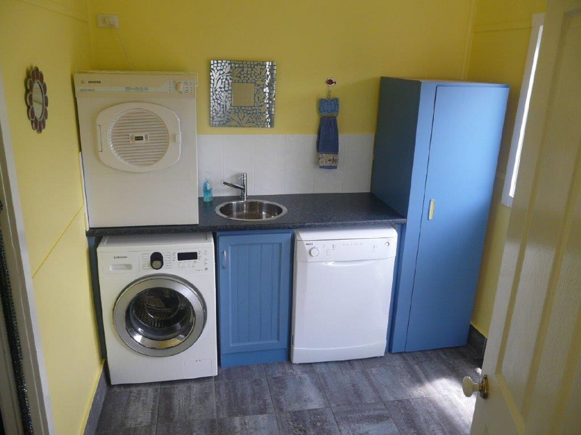 Une cuisine compacte équipée d’un lave-linge, d’un lave-vaisselle, d’un évier et d’un miroir décoratif.